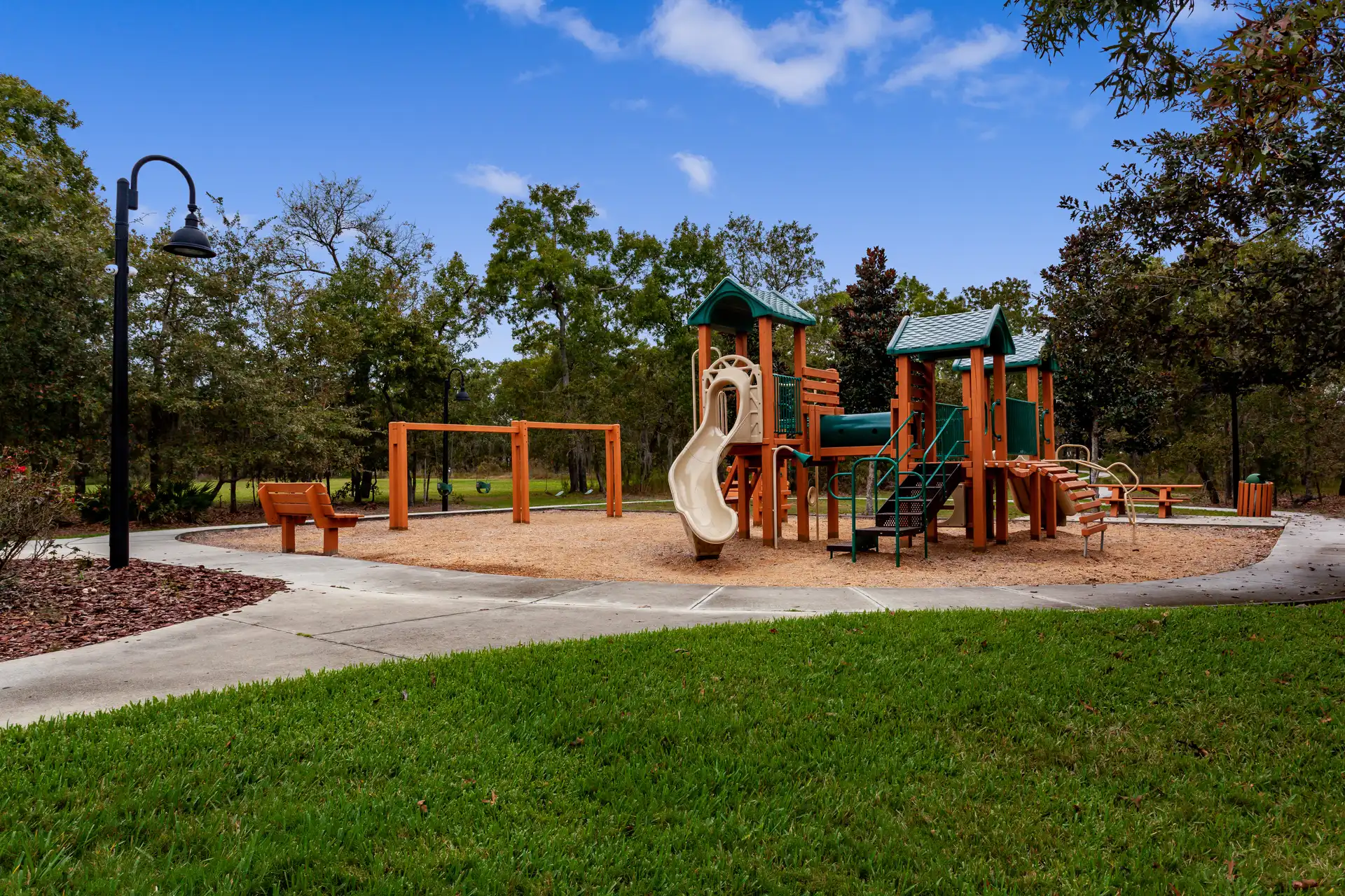 Leerer Spielplatz mit orangegruenem Klettergeraet und Rutsche unter blauem Himmel