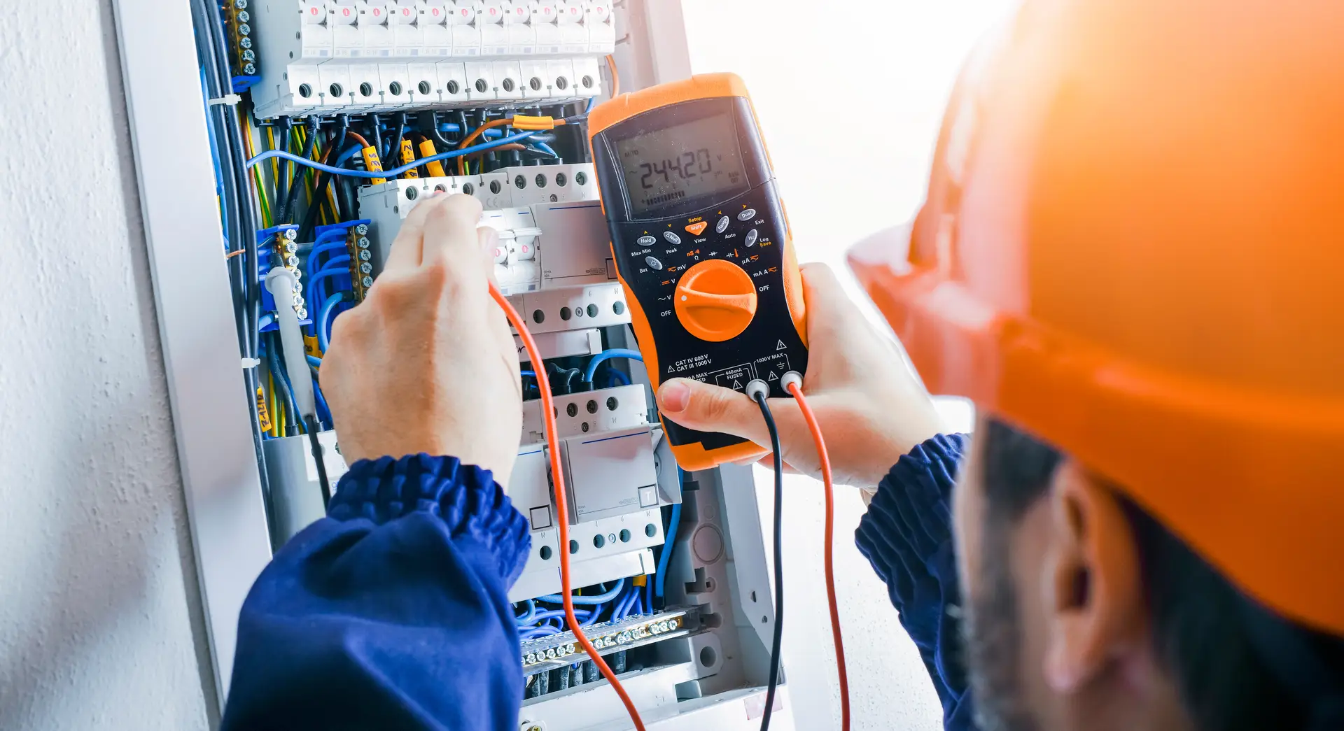 Elektriker mit konzentriertem Blick misst im Schaltschrank mit orangefarbenem Multimeter