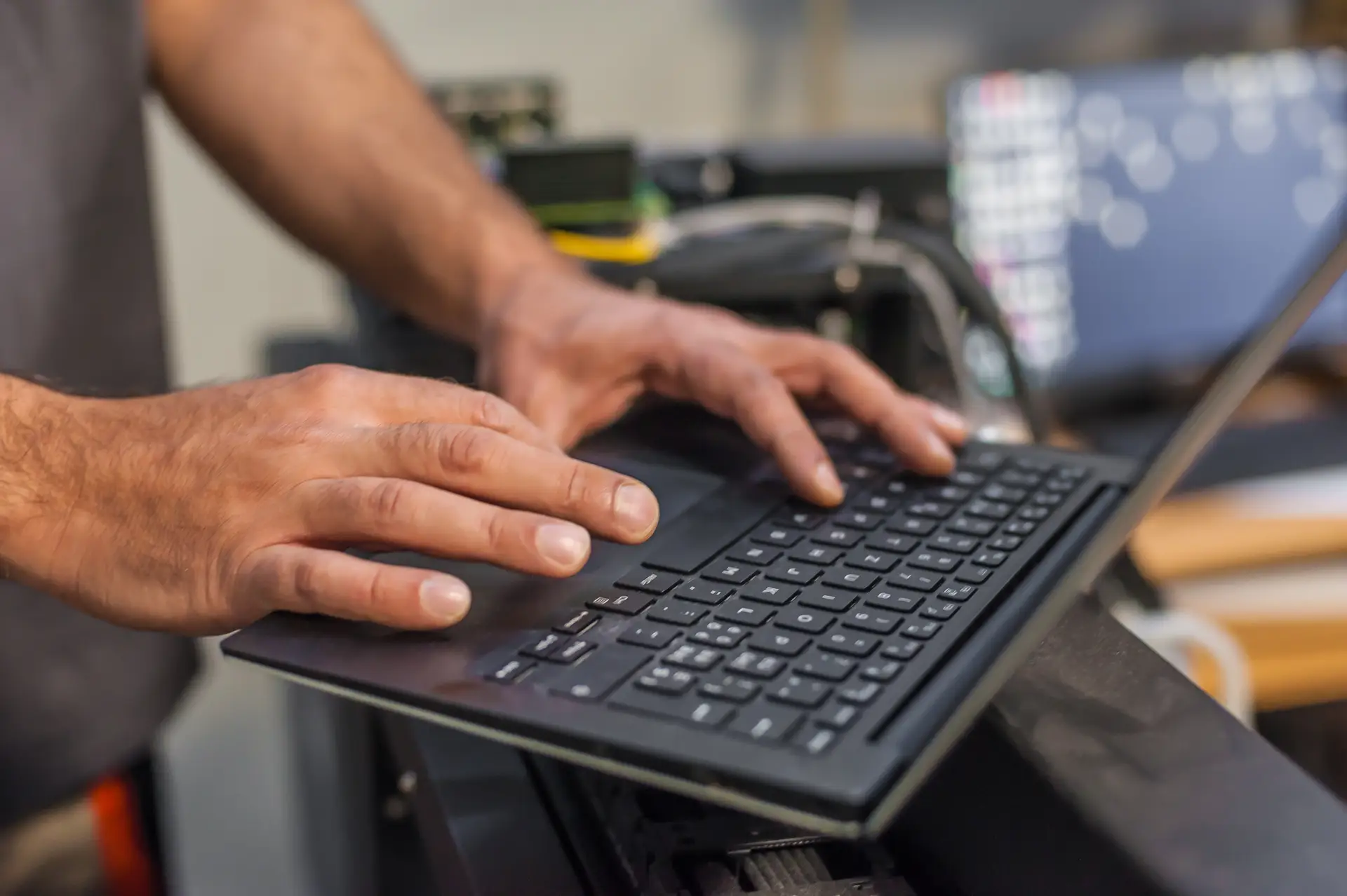 Neutrale Haende tippen auf schwarzer Tastatur mit Kabeln im Hintergrund